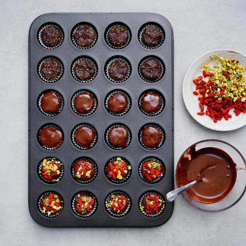 Topping brownie cups with melted chocolate and goji berries