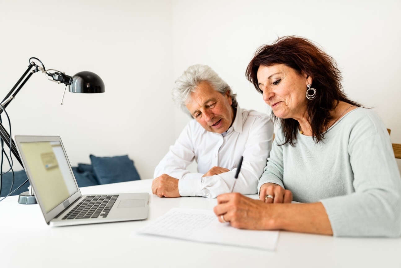 Senior couple sitting at a table, engrossed in paperwork, at the comfort of their home
