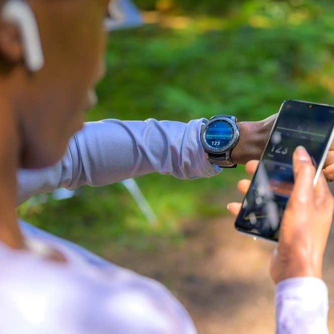 Person checking activity data on a smartwatch while holding a smartphone outdoors.