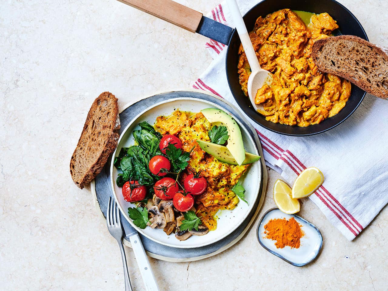 Plate of turmeric scrambled eggs next to a cooking pan with more cooked turmeric scrambled eggs.