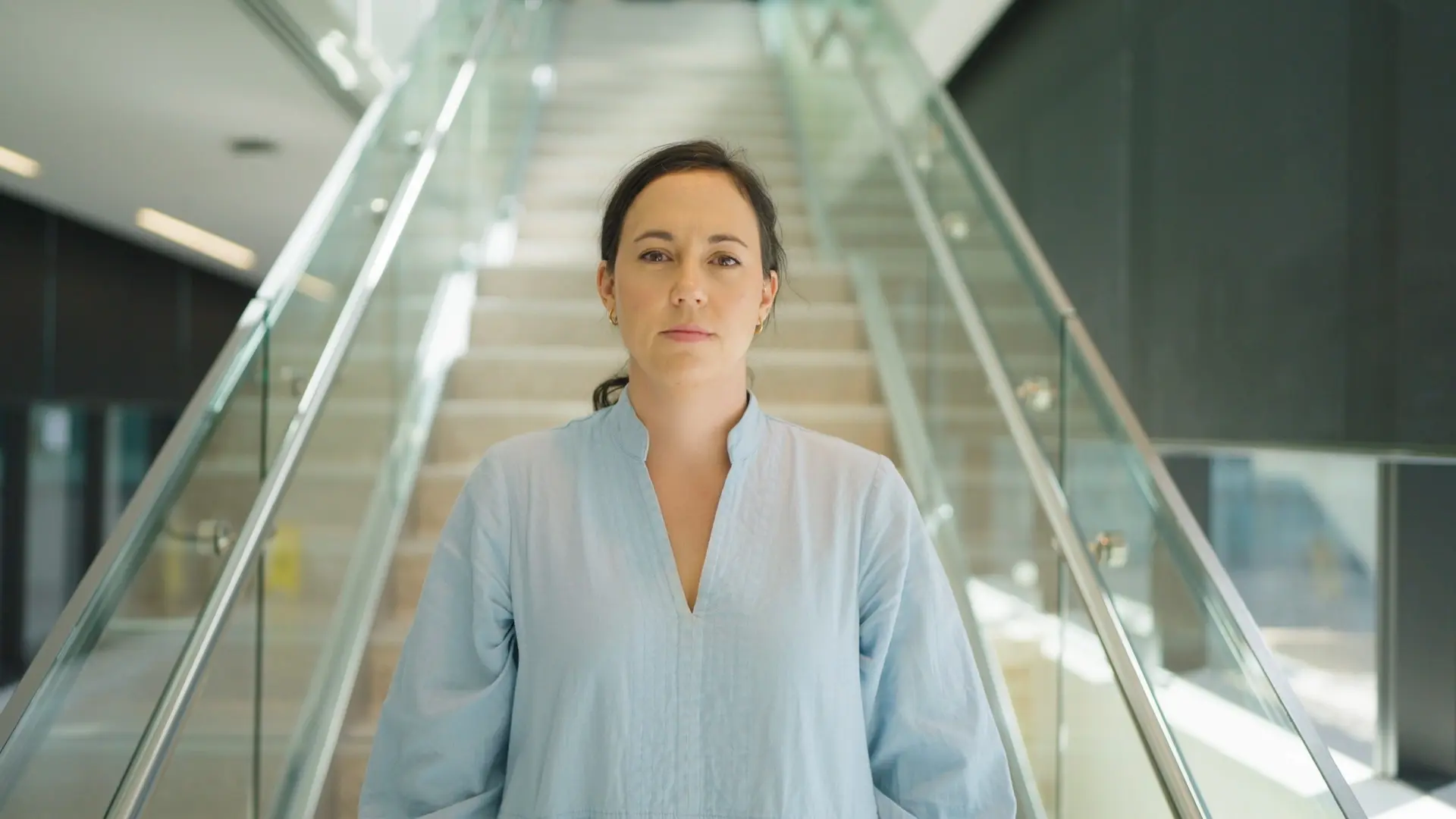 Dr Holly Voges standing looking into camera in front of a stairway