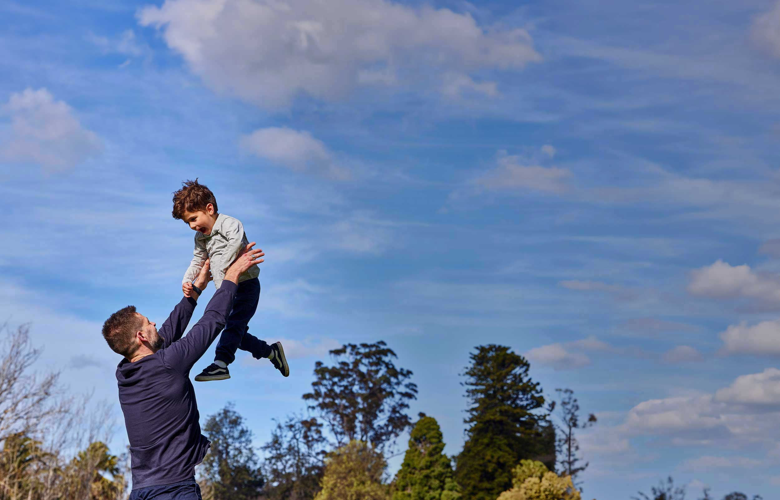 A man is throwing his young son up in the air in a park
