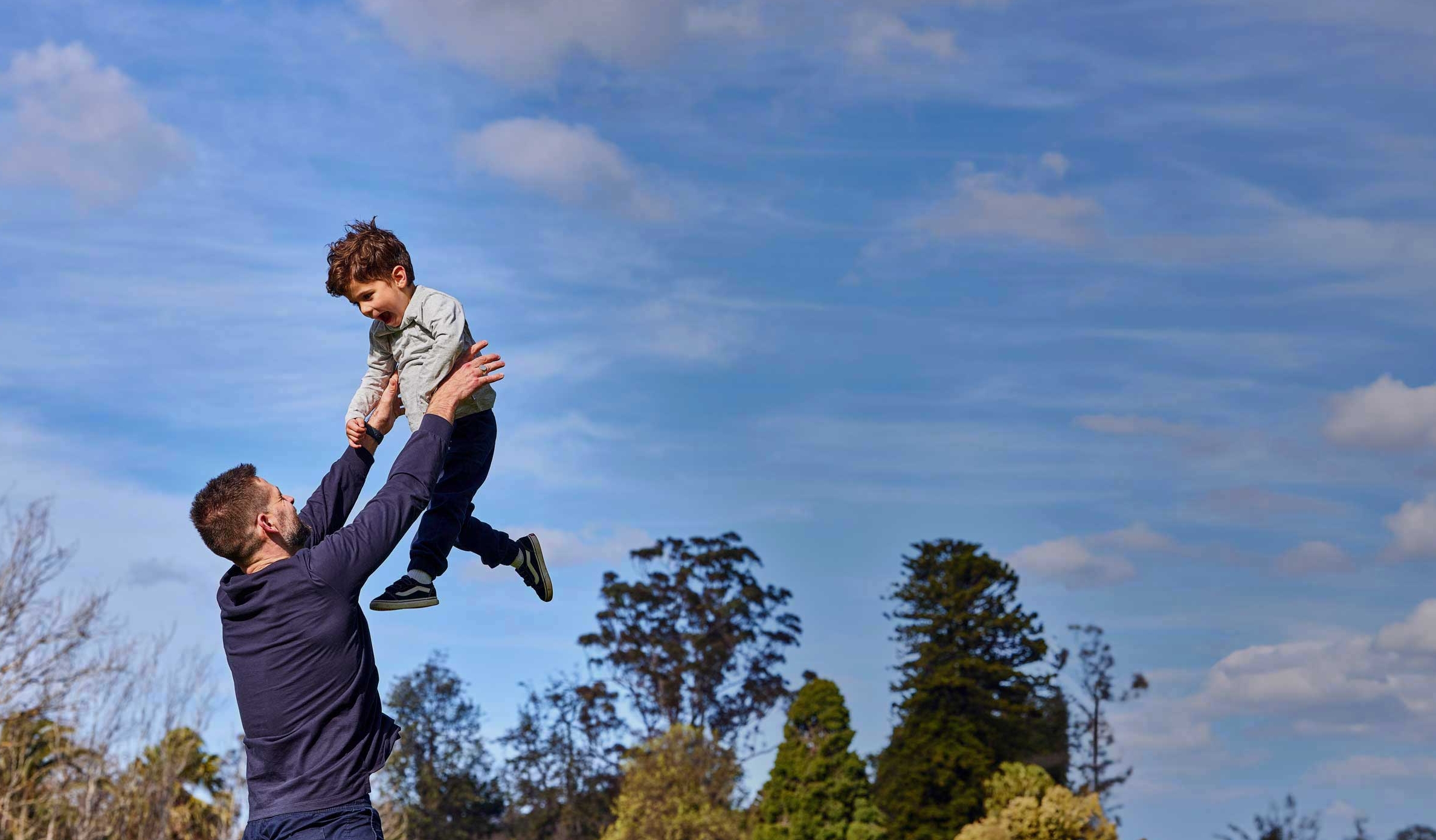 A man is throwing his young son up in the air in a park