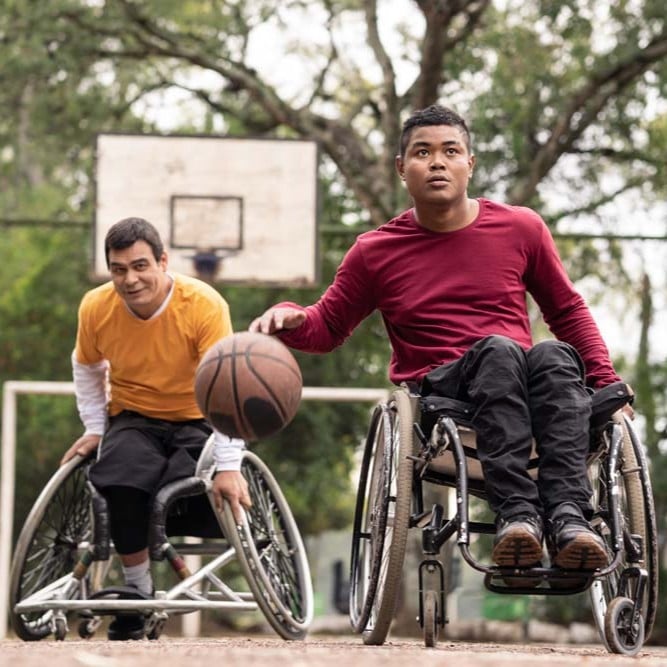 Two wheelchair users playing basketball on an outdoor court.