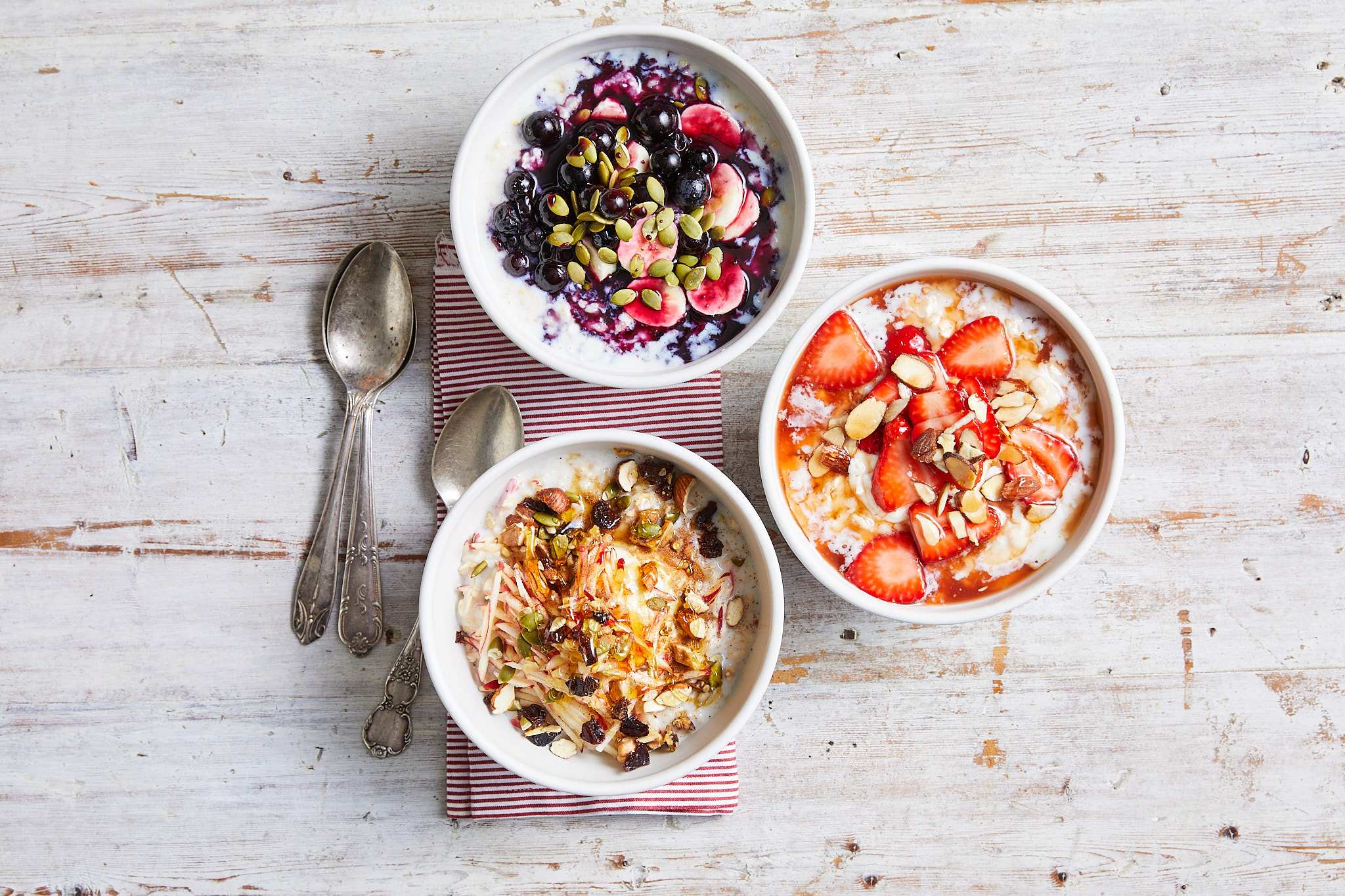 Three bowls of oatmeal topped with fruit and nuts