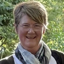 A smiling woman wearing glasses and a scarf.