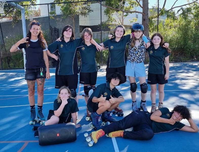 A group of students and their coach posing on a sports court in roller skates