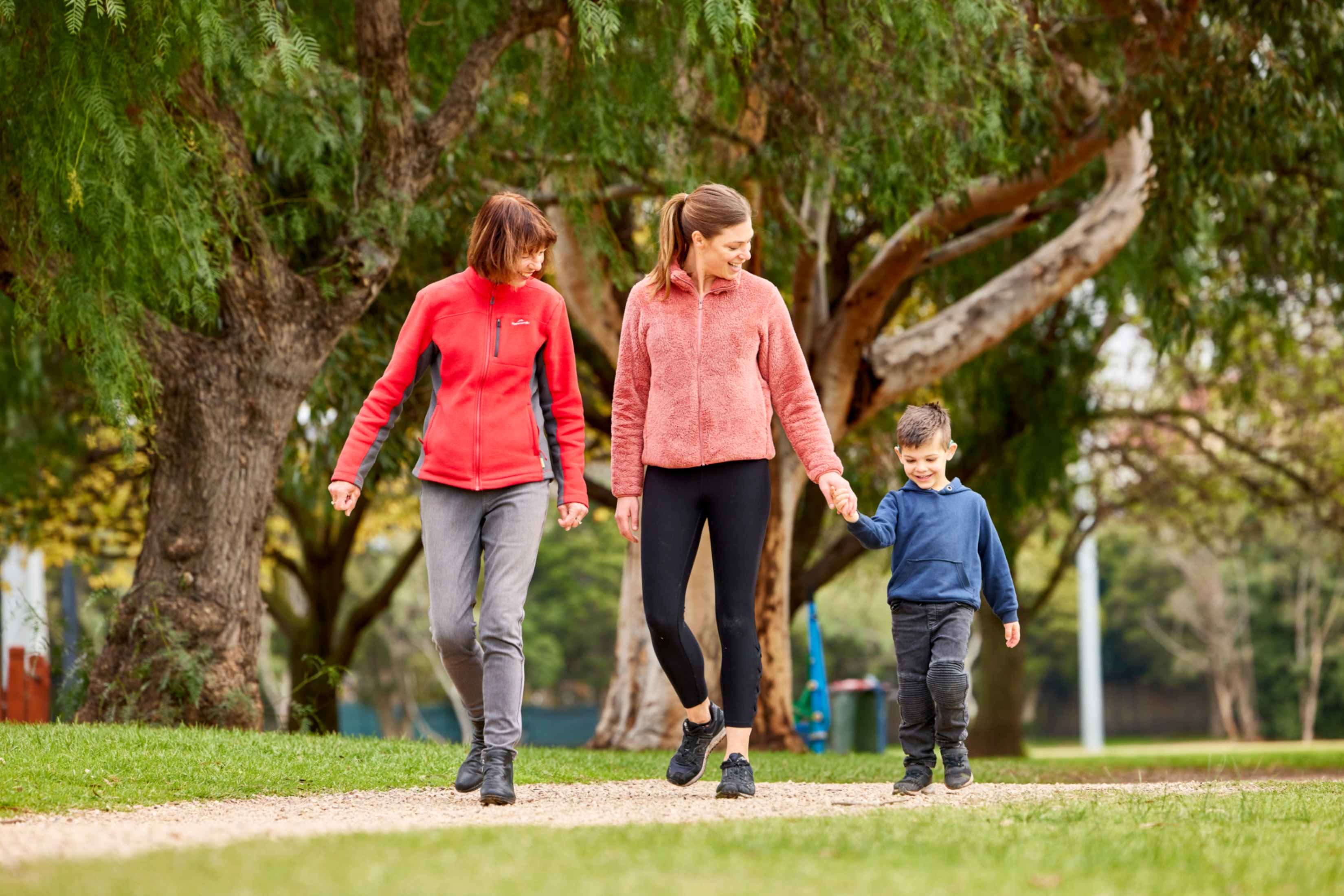 A family, including a grandmother, mother and son, walking through a park