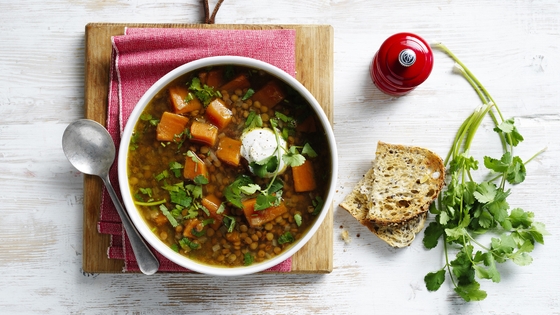 Asian-spiced sweet potato and lentil soup in a bowl on a chopping board with bread on the side