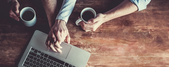 Two individuals holding hands over a laptop and coffee, symbolising connection