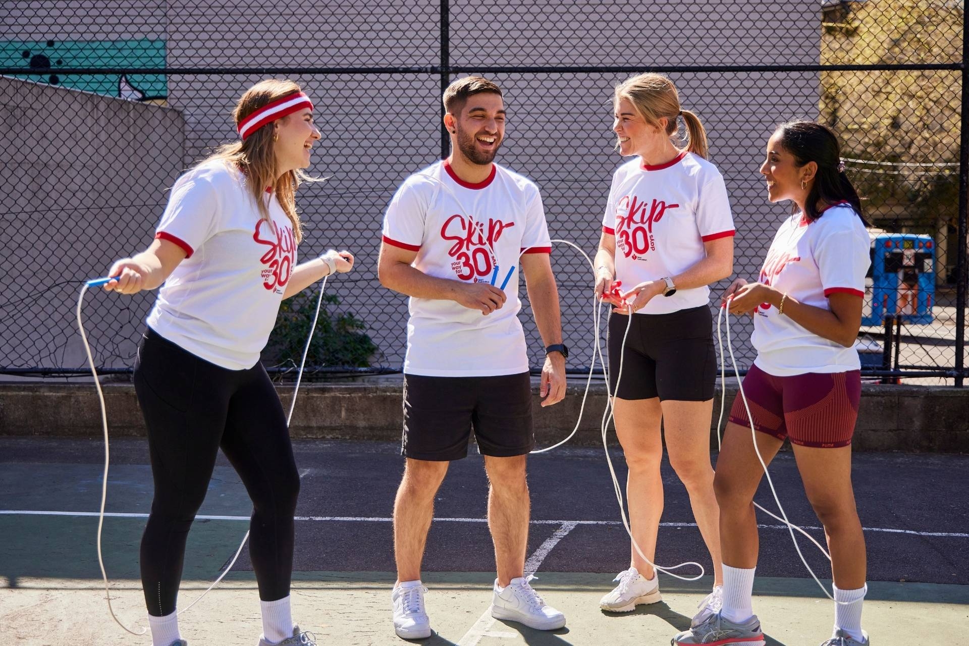 A group of four people standing with skipping ropes, wearing t-shirts for Skip Your Way for 30 Days