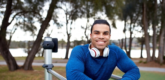 A young man wearing headphones, sitting on a bench and smiling.