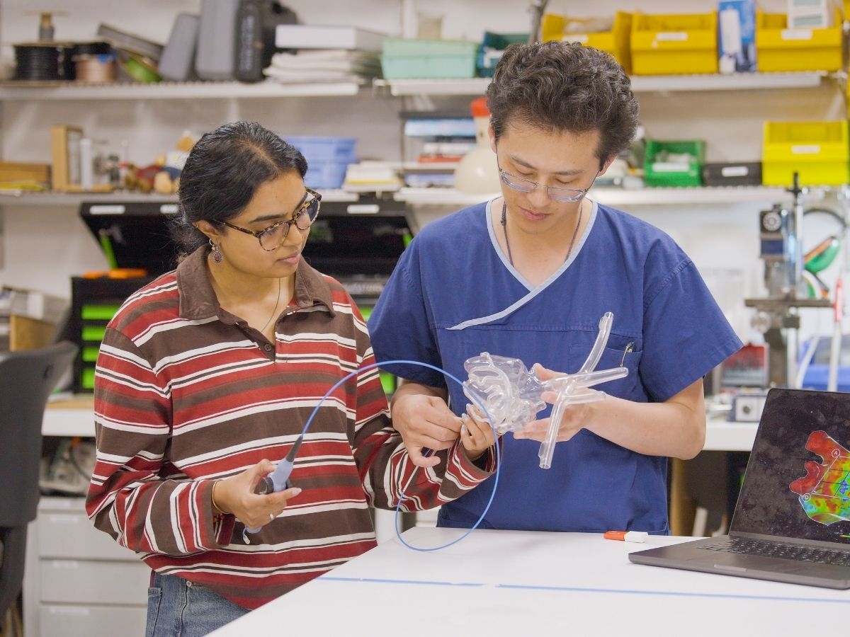 Two researchers in a lab examining a transparent anatomical heart model, surrounded by equipment and a laptop displaying related visuals.
