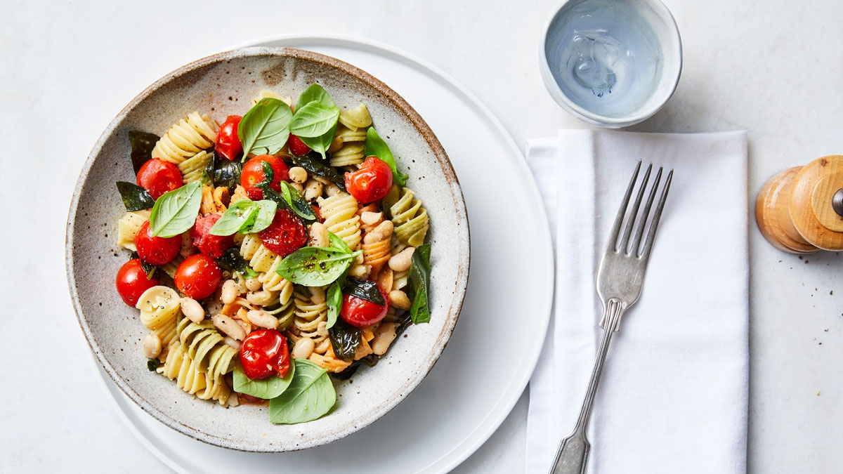 A delectable bowl of pasta adorned with vibrant tomatoes, fresh spinach, and fragrant basil leaves