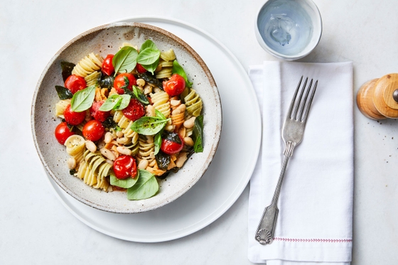 A delectable bowl of pasta adorned with vibrant tomatoes, fresh spinach, and fragrant basil leaves
