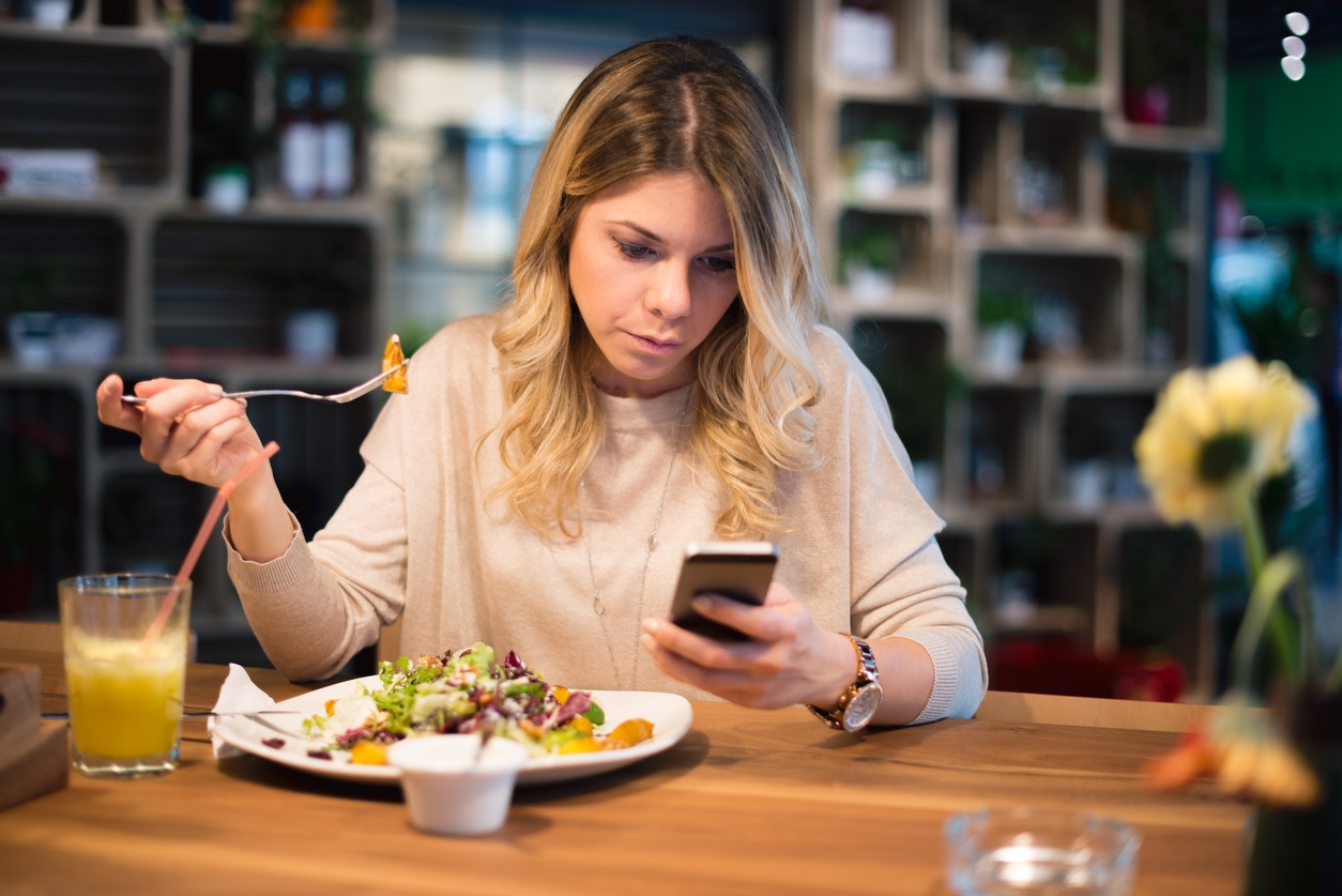 Woman multitasking: eating salad and checking phone