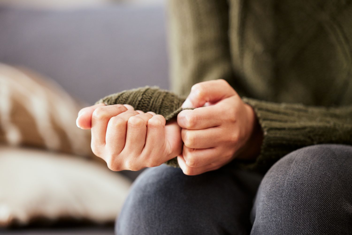 Close-up of a person sitting with hands clasping the sleeve of a knitted jumper, resting on their lap.