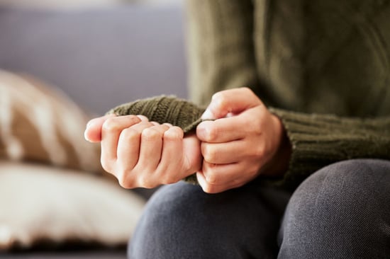 Close-up of a person sitting with hands clasping the sleeve of a knitted jumper, resting on their lap.