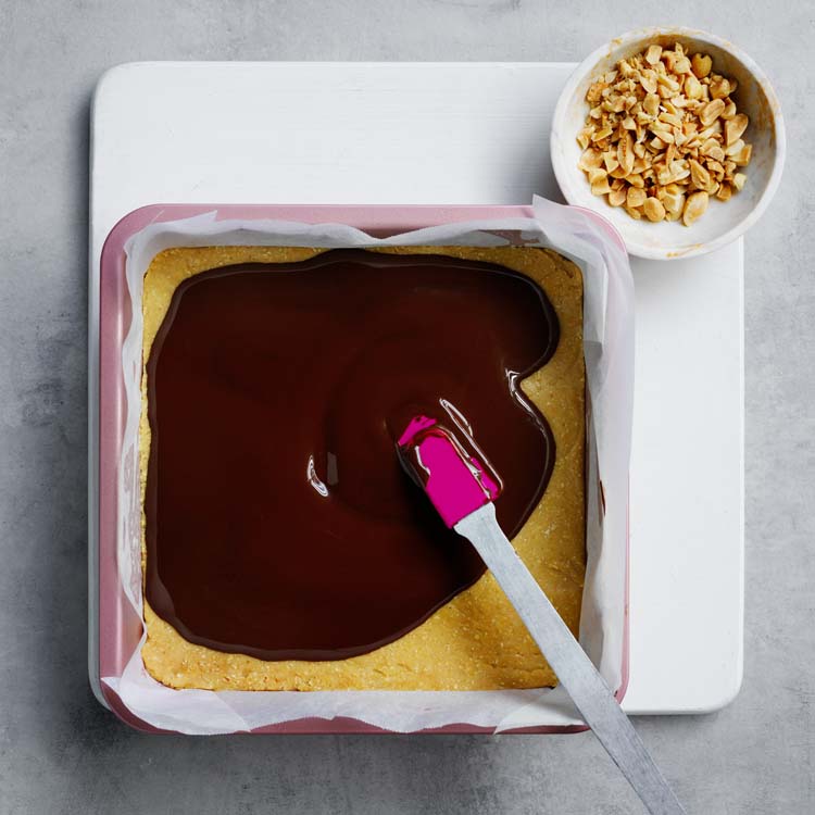 Melted chocolate poured over the slice base and sprinkled with peanuts