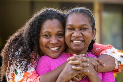 Indigenous woman smiling with arms around younger woman smiling