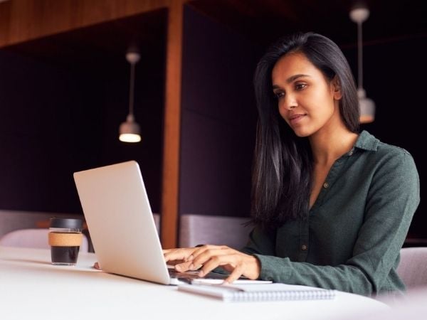 Woman typing on laptop with coffee