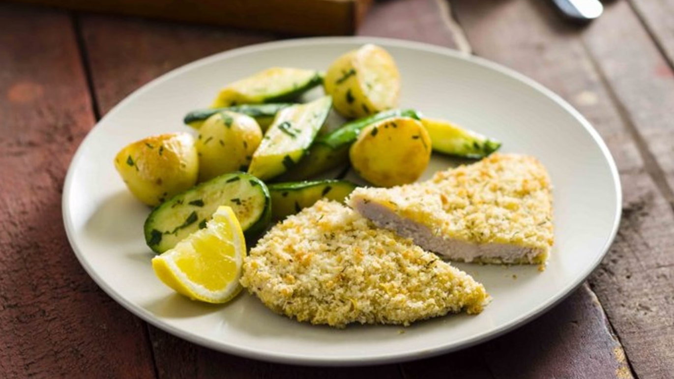 Oven baked chicken schnitzel plated up with potato and zucchini and a slice of lemon