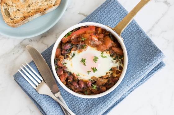 A skillet filled with eggs, beans, tomatoes with grainy toast, creating a colorful and appetizing dish.
