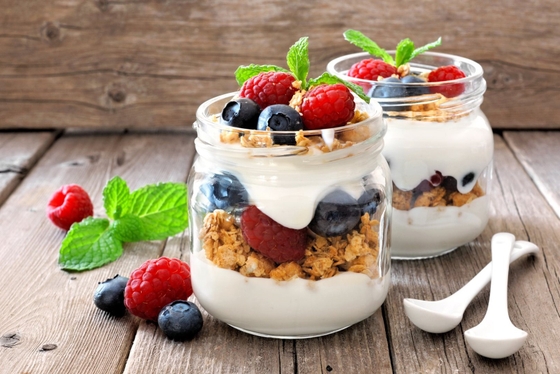 Yogurt, berries, and granola beautifully presented in glass jars on a rustic wooden table.