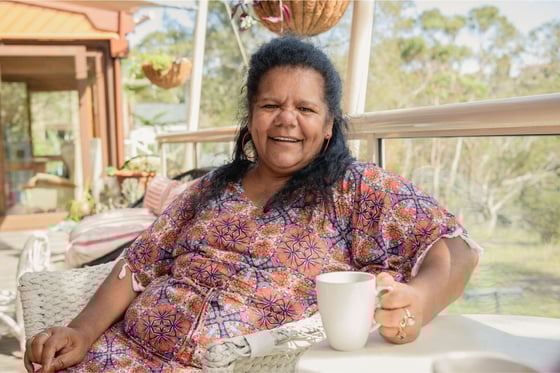 Woman sitting outside with mug and smiling towards camera