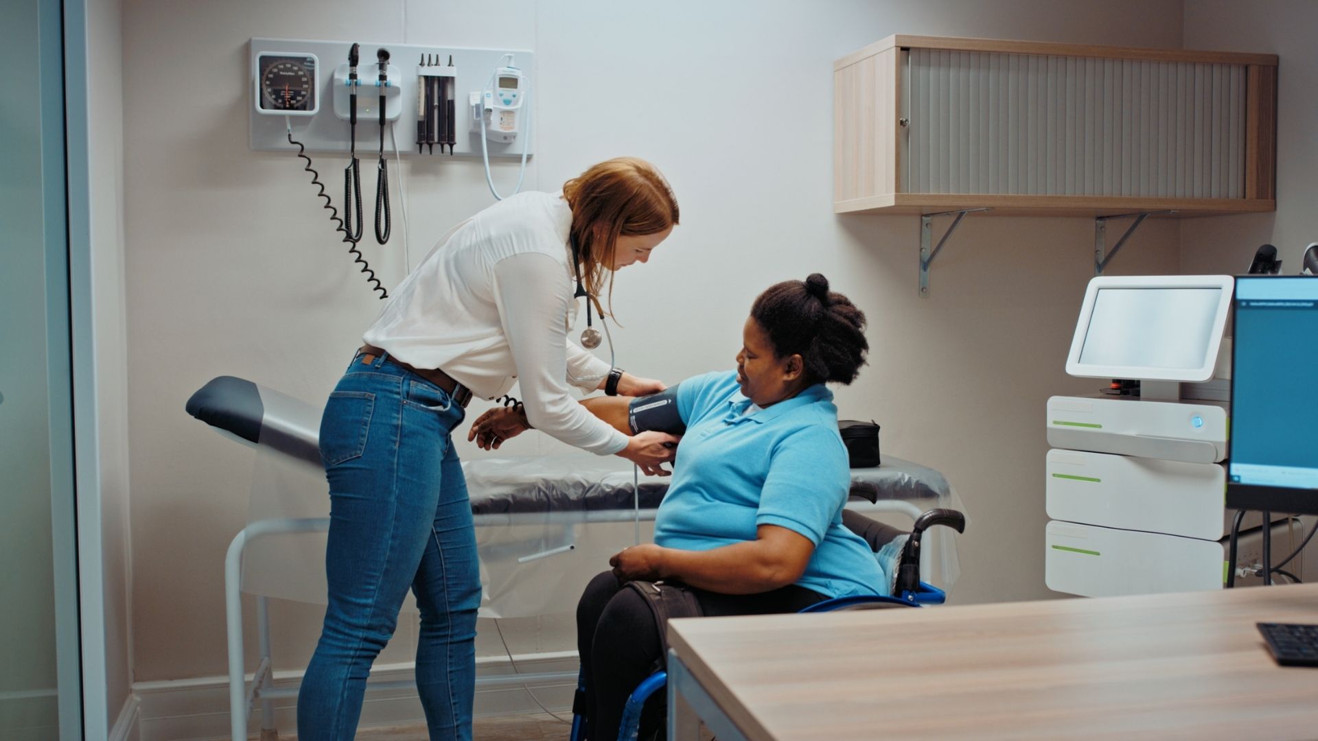 A female doctor checking the blood pressure of a patient who is using a wheelchair