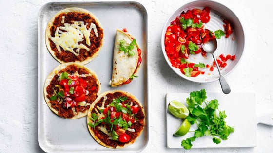 Smashed bean tacos on tray and bowl of tomato salsa and lime next to it