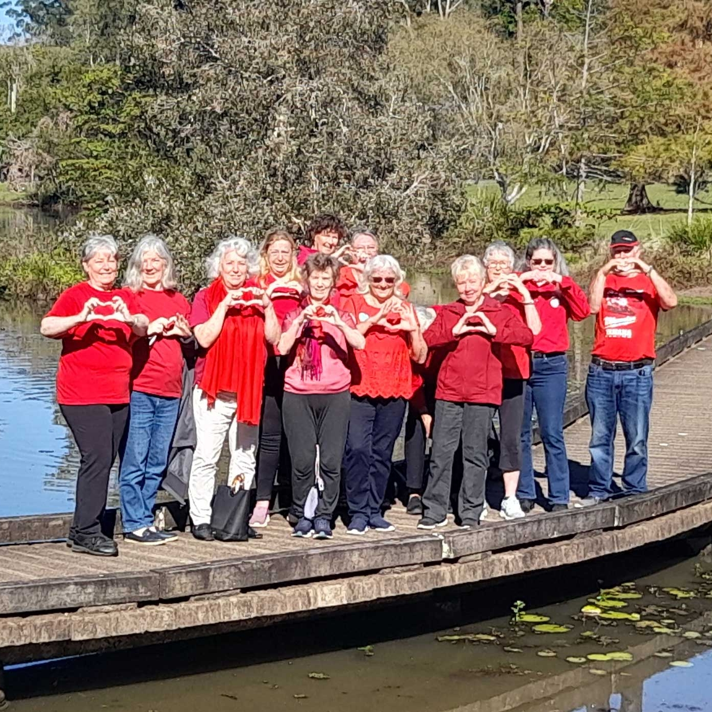 Mapleton Movers 12 people in red t-shirts making heart symbol with their hands, standing on a bridge 