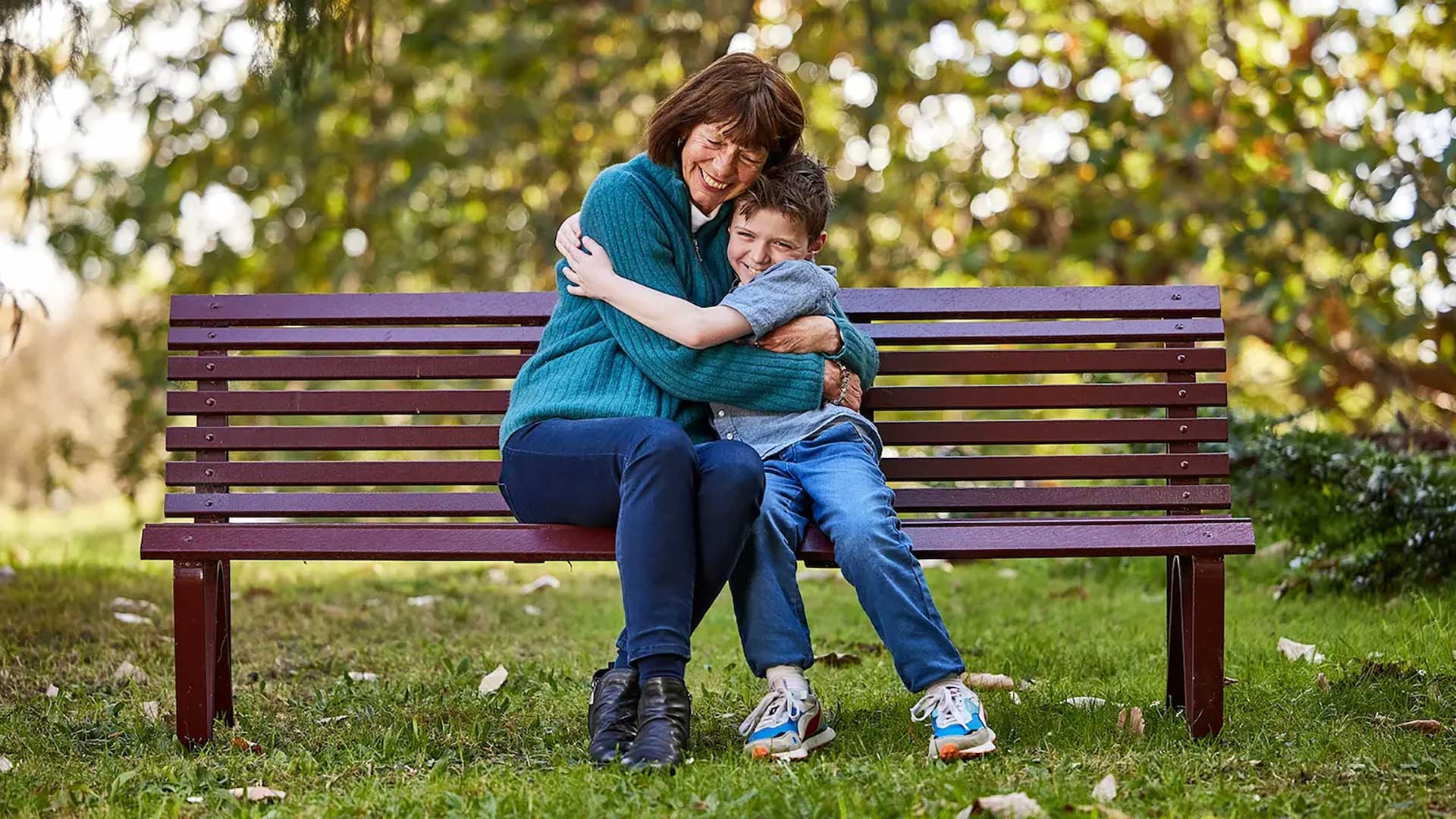 Mature woman hugging her grandson on a park bench