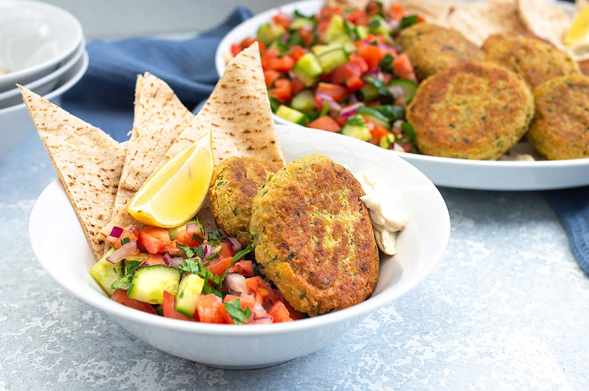 Two bowls of food with pita chips and vegetables