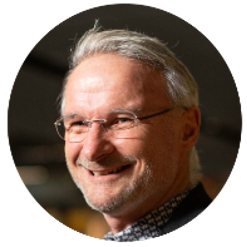 A professional man wearing glasses and a suit, displaying a warm smile.