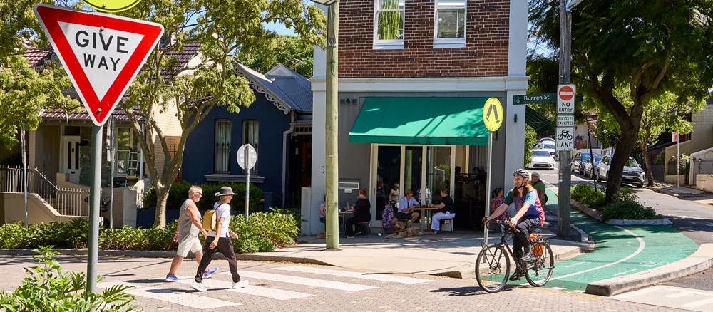 People walking and cycling through a neighbourhood street with a pedestrian crossing and separated bike lane.