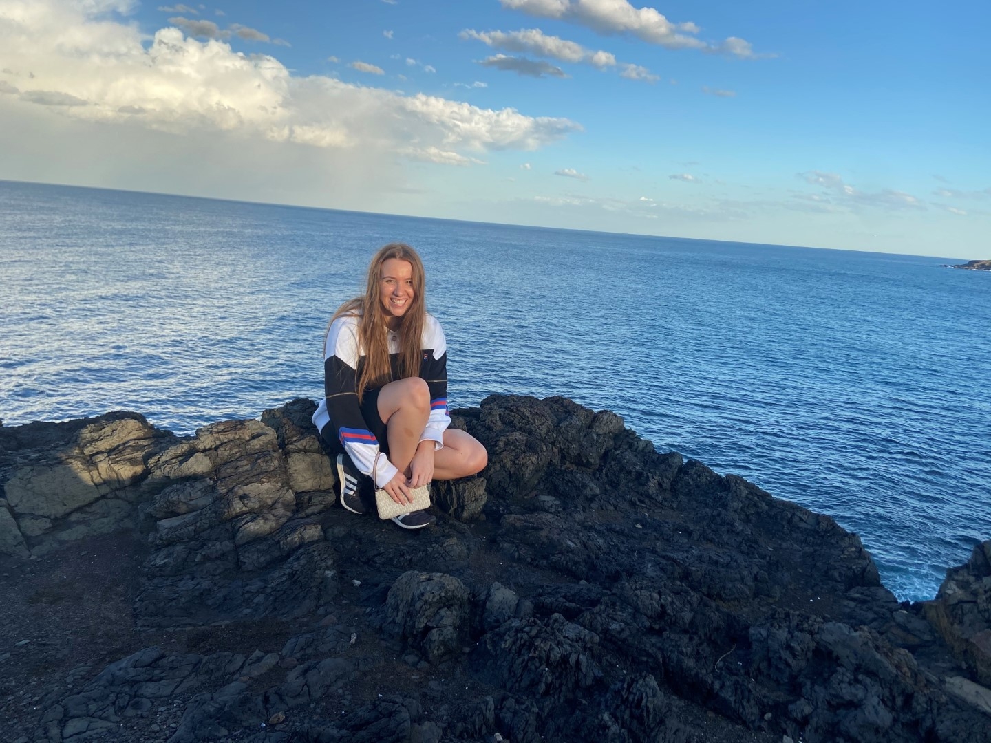 picture of smiling bianca beetham sitting on stone besides beach