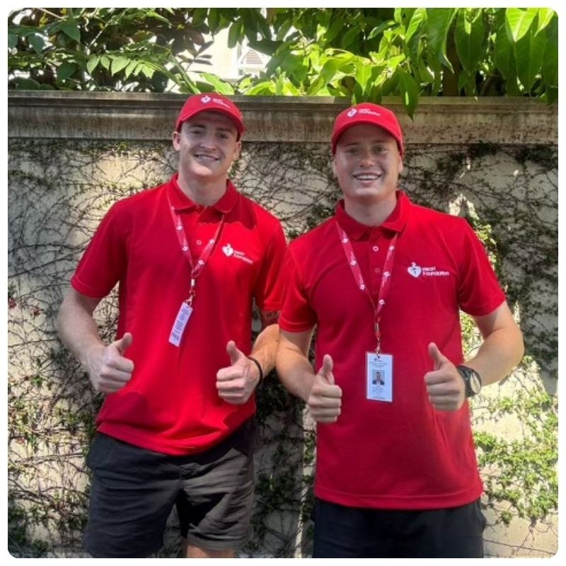 Two friendly Heart Foundation fundraisers walking down the street, in red polo and red caps