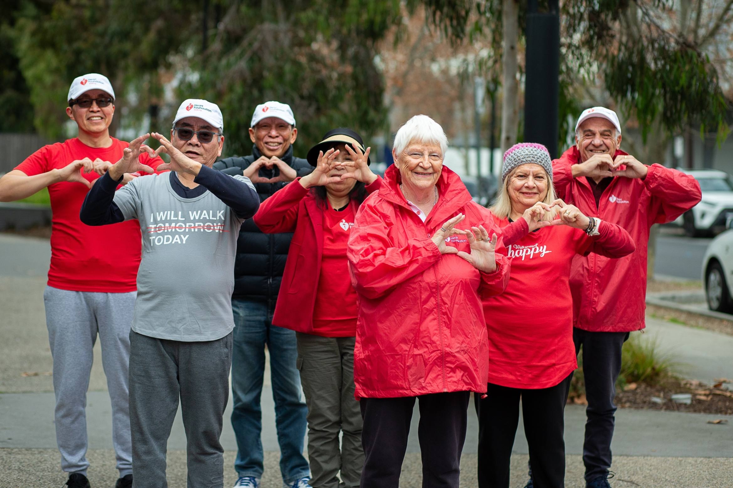 A group of smiling people wearing Heart Foundation shirts and holding up their hands in the shape of hearts