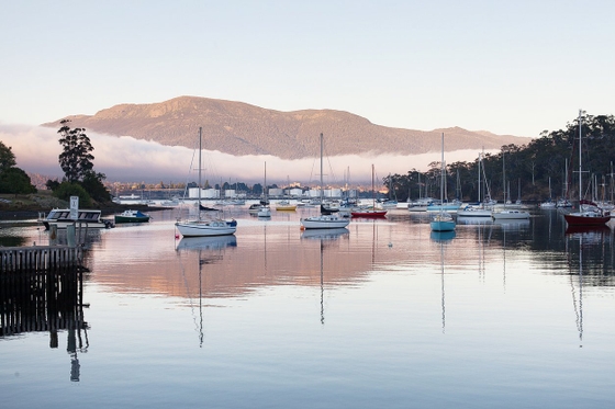 Boats docked near mountains, reflecting on calm water. A serene scene of nature's beauty.