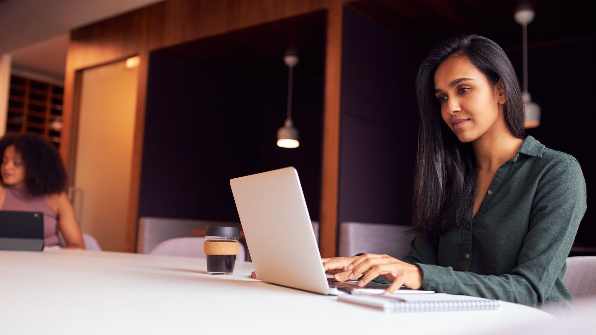 Woman sitting at table typing on laptop with a coffee nearby