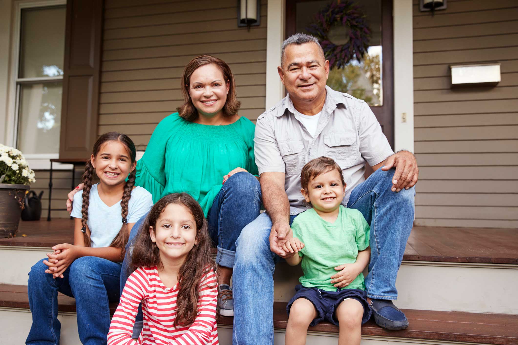 Family of five (male & female parents and three kids) sitting on steps of their house, smiling