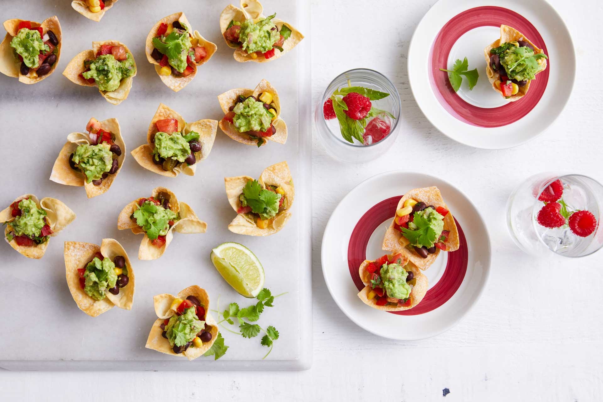 Serving board with open cup shaped wonton wrappers filled with a mix of fresh salad veggies and herbs, with coriander and lemon, a delicious appetizer.