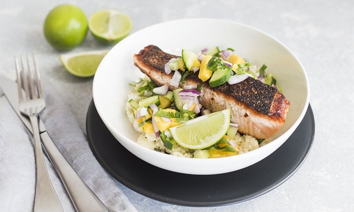 A dish of fish, rice and lime wedges on a plate.