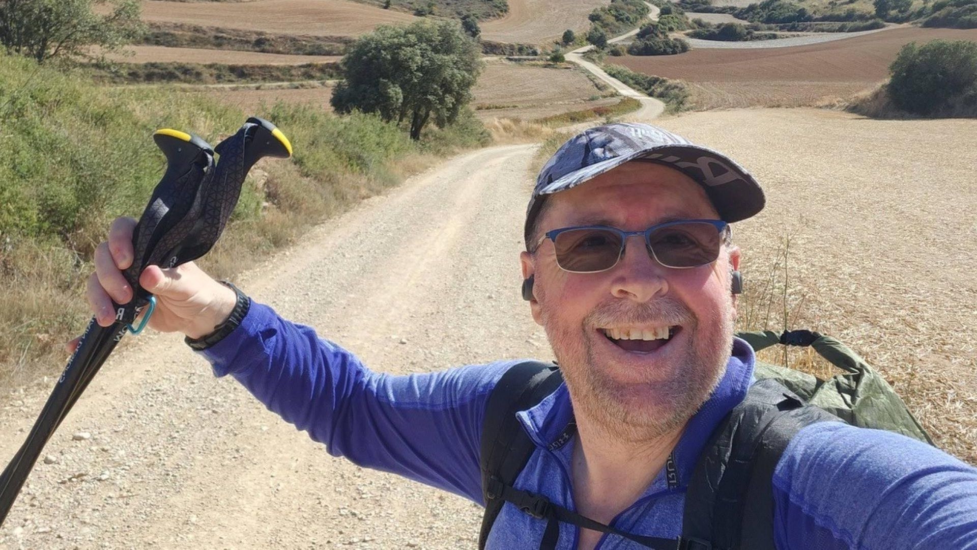 Phillip, holding a hiking stick and walking through the countryside