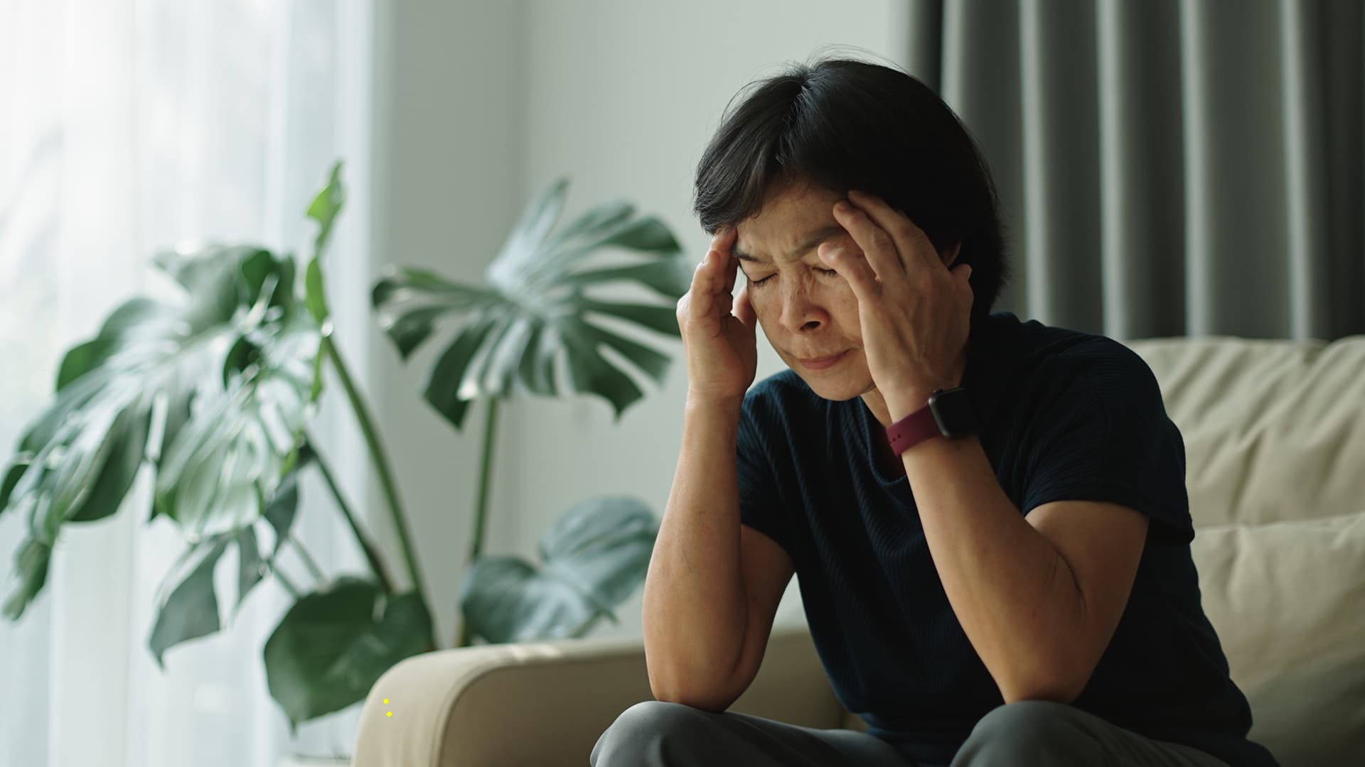 Mature woman with dark hair is sitting holding her temples feeling dizzy or faint