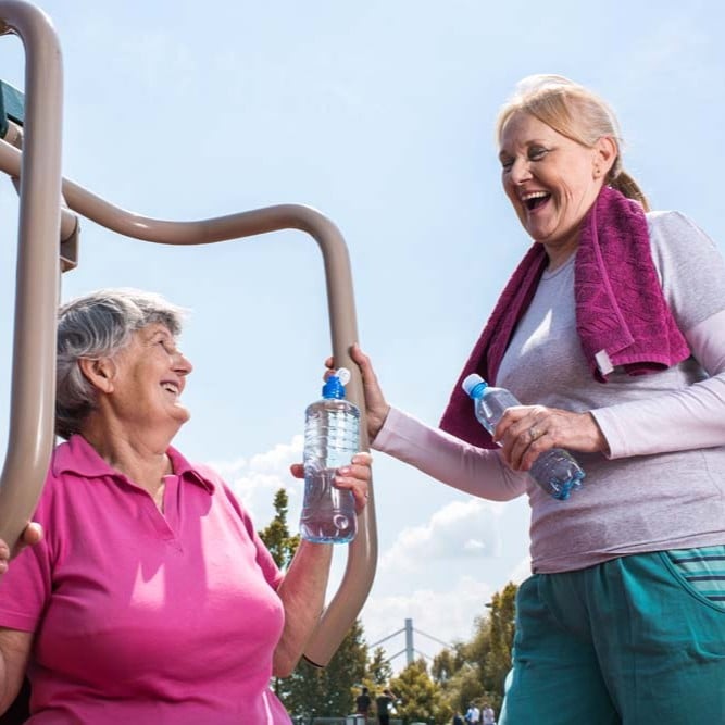 Two older adults using outdoor fitness equipment in a public park