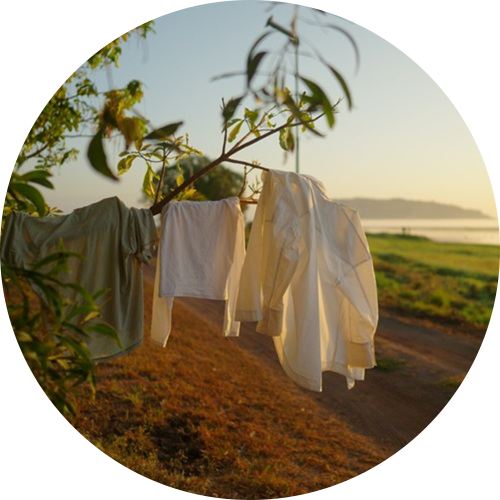 Clothes hanging on an outdoor washing line beside a dirt track and coastline at sunrise.