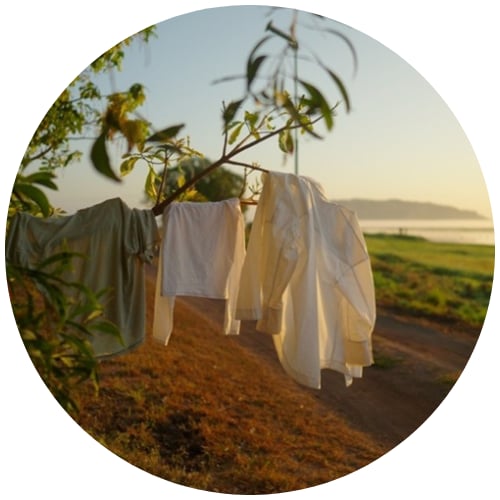 Clothes hanging on an outdoor washing line beside a dirt track and coastline at sunrise.