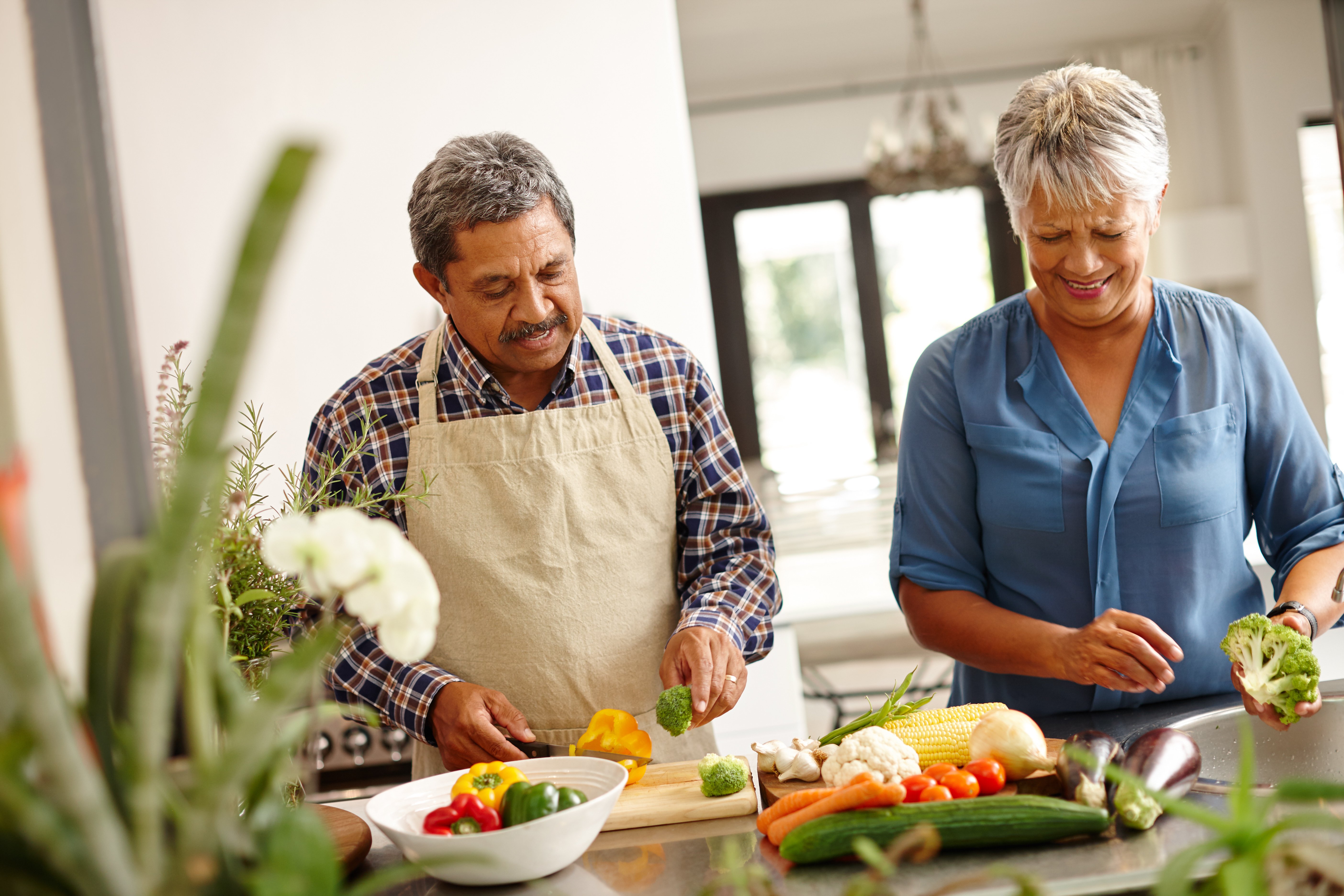 Man and woman with gray hair standing cooking a healthy meal in the kitchen smiling